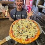 A picture of a pizza pie with an excited employee from Pizza Palace Wellington
