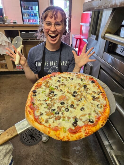 A picture of a pizza pie with an excited employee from Pizza Palace Wellington
